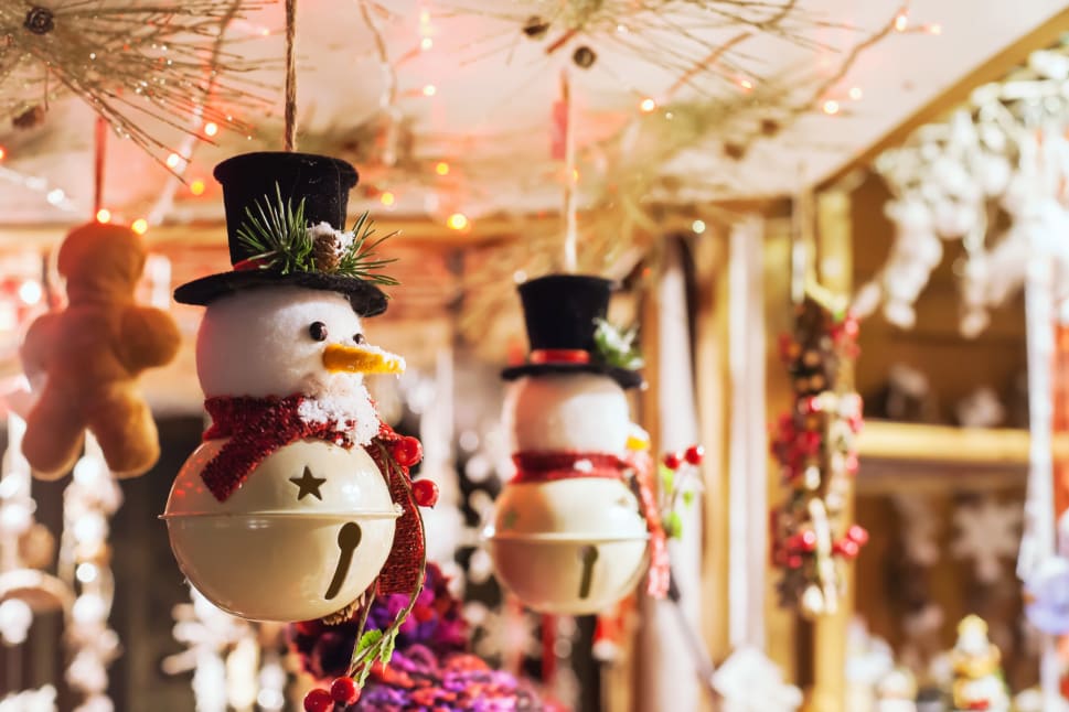 Festive snowman ornaments wearing black hats and red scarves hanging from a decorated ceiling with warm lights.