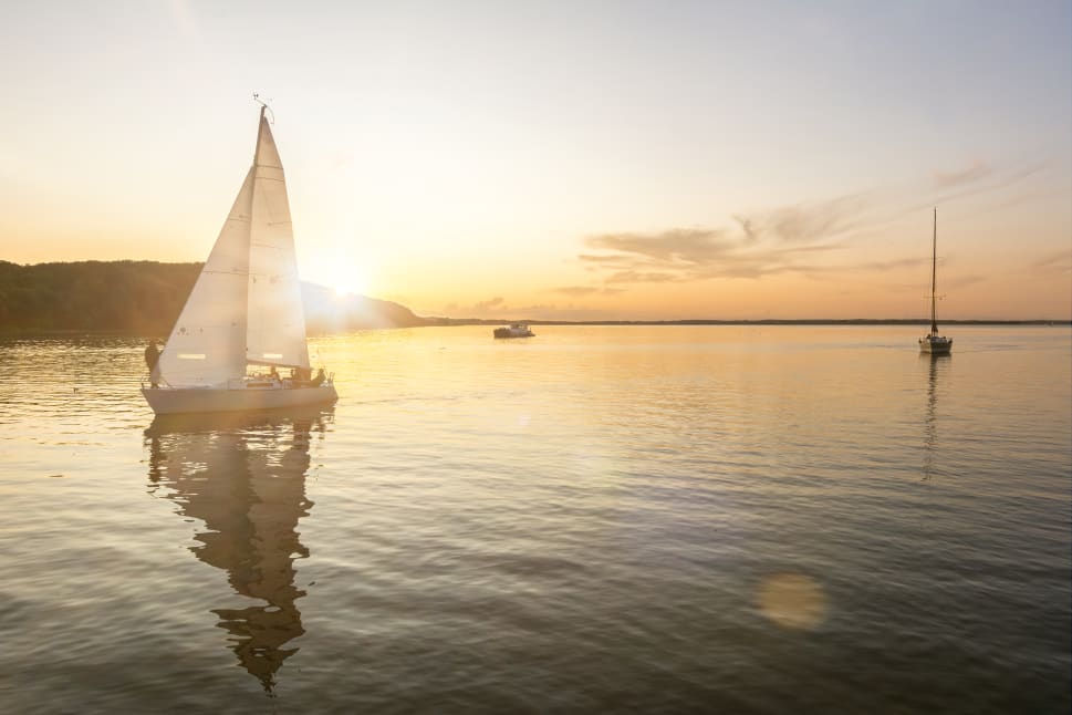 A sailboat on a calm lake during sunset with another boat in the distance.