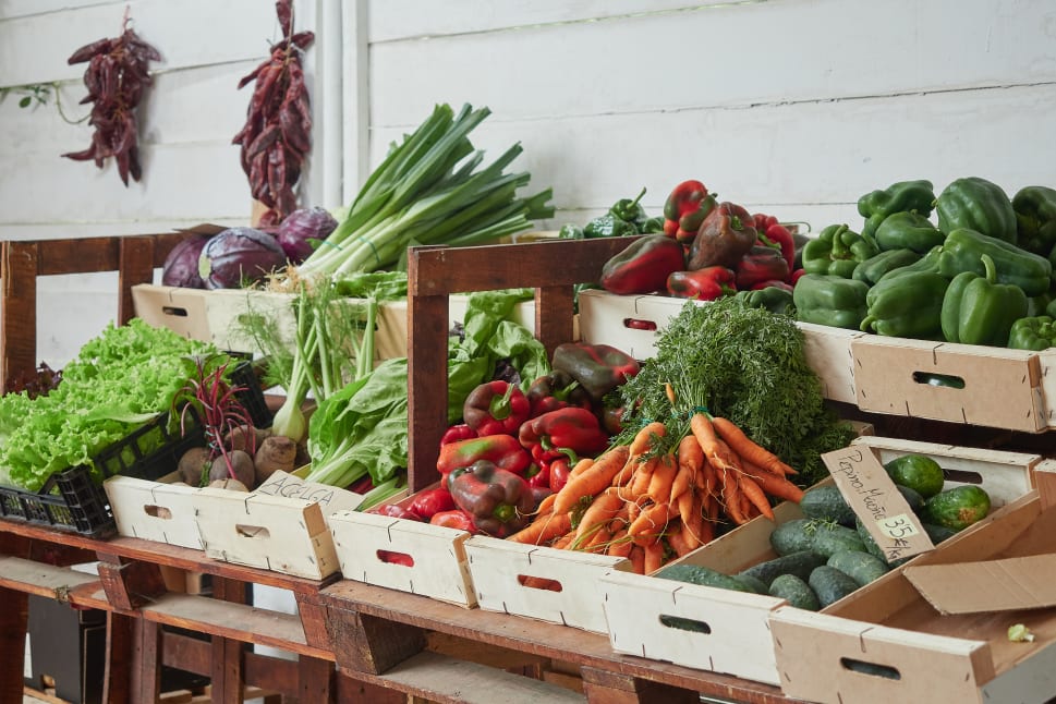 Fresh produce including carrots, green peppers, and leeks displayed in wooden crates at a farmers market stall.