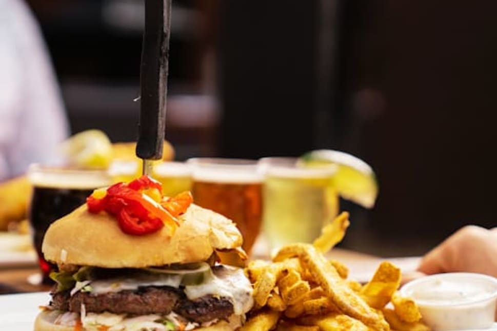 A gourmet burger with fries on a white plate, with various craft beers in the background at Barley Mill Brew Pub in Penticton.