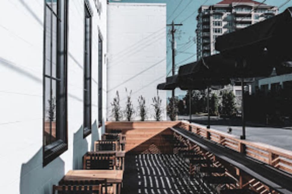 Outdoor patio at Wayne-Freda Cafe in Penticton, featuring wooden tables and chairs under a clear blue sky with building and power lines in the background.