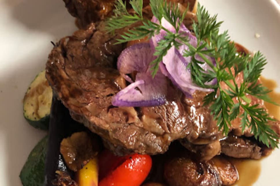 A plate of Cajun-Creole dish with steak slices, roasted vegetables, and garnished with fresh herbs at Bourbon Street Bar and Grill in Vernon.