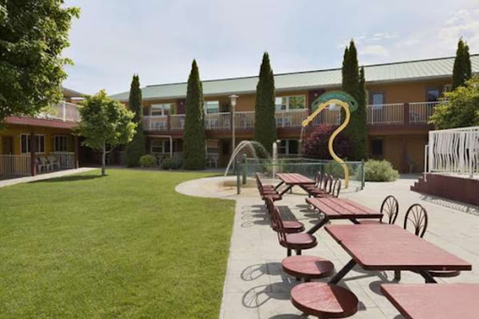 Outdoor courtyard at Days Inn by Wyndham Penticton Conference Centre with picnic tables, trees, and a yellow playground slide.