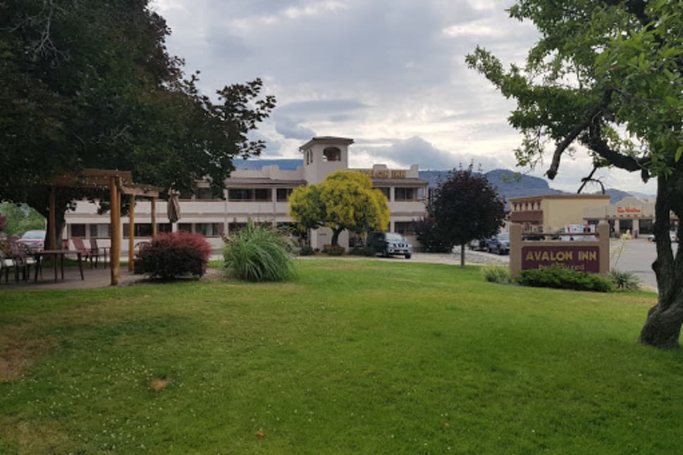 Exterior view of Avalon Inn showing a green lawn, trees, and a motel building with a sign labeled "Avalon Inn" in Osoyoos, British Columbia.