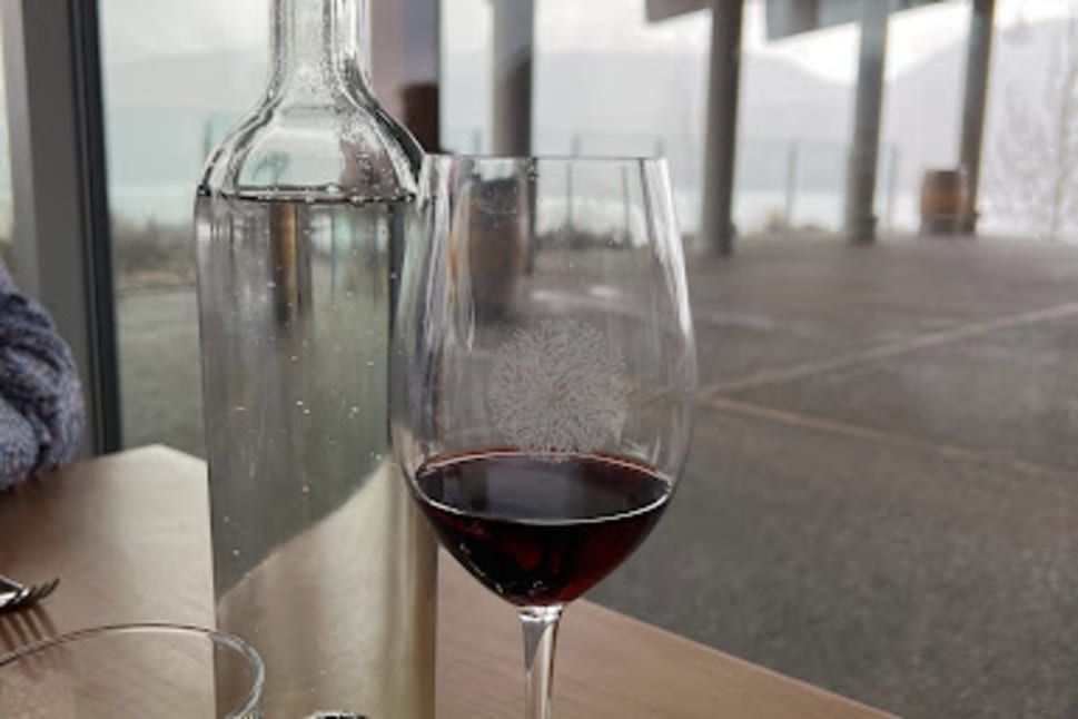 A glass of red wine, an empty water glass, and a partially filled water bottle on a wooden table with a scenic view in the background at Poplar Grove Winery.
