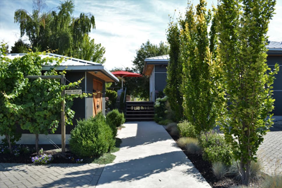 A charming outdoor view of 8th Generation Vineyard in Summerland, featuring a walkway lined with lush greenery and a sign reading "Wine Shop."