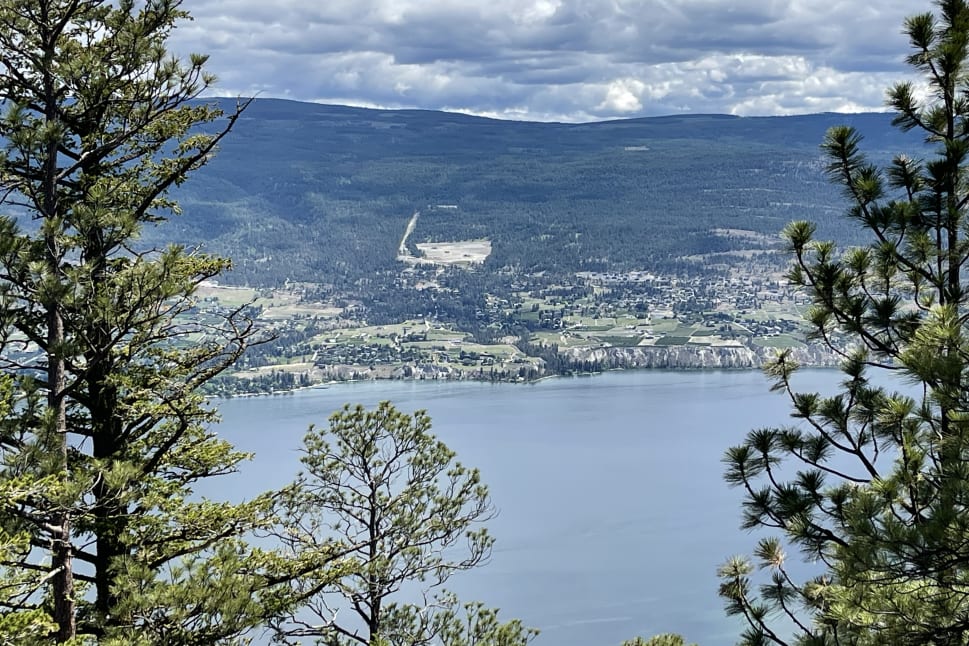 A scenic view of Summerland with green hills, clouds in the sky, and a lake surrounded by trees.