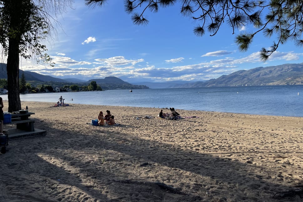 People enjoying a sunny day at Summerland beach with mountains in the background and a clear blue sky.