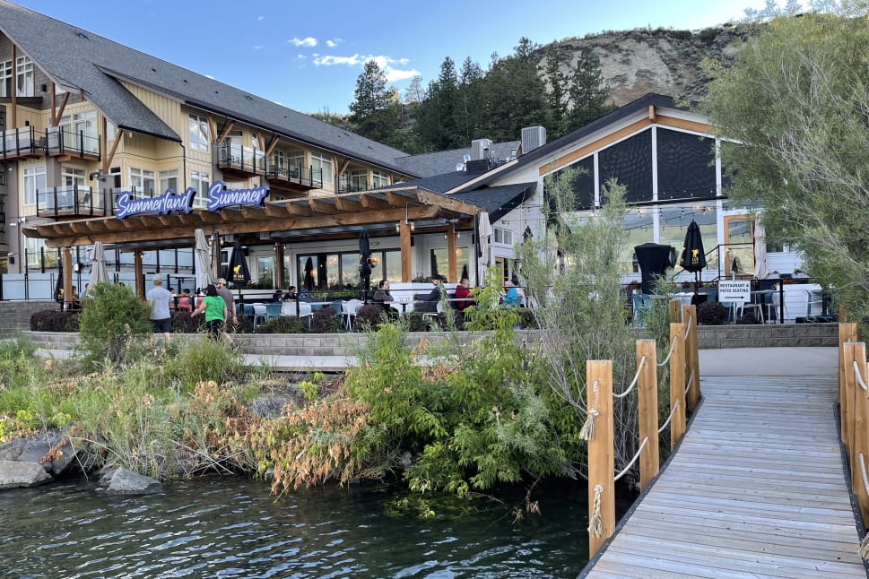 A scenic lakeside restaurant named "Summerland Summer" with outdoor seating, near a wooden dock and surrounded by greenery.