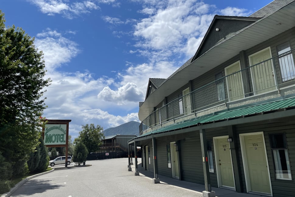 Summerland Motel exterior with a clear blue sky and mountain in the background, showcasing a parking lot and a sign for the motel.