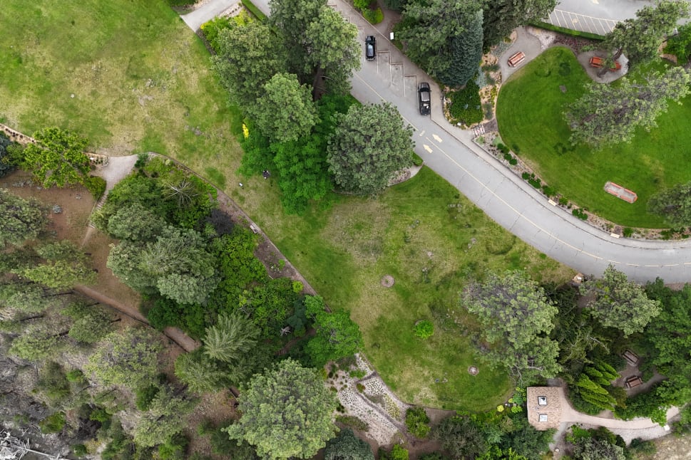 Aerial view of a green park with trees, paths, and parked cars along a curved road in Summerland.