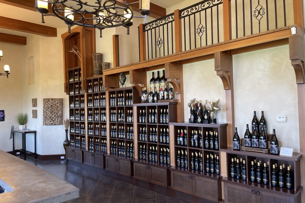 A wine tasting room in Osoyoos showcasing a large wooden shelving unit filled with various bottles of wine, elegant chandeliers hanging from the ceiling.