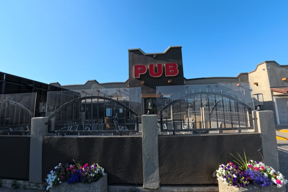A pub in Osoyoos on a sunny day with clear skies, featuring an outdoor seating area with an arch gate and concrete planters with colorful flowers.