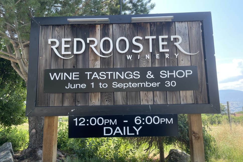A sign for Red Rooster Winery in Penticton advertising wine tastings and shop open daily from June 1 to September 30, 12:00 PM to 6:00 PM.