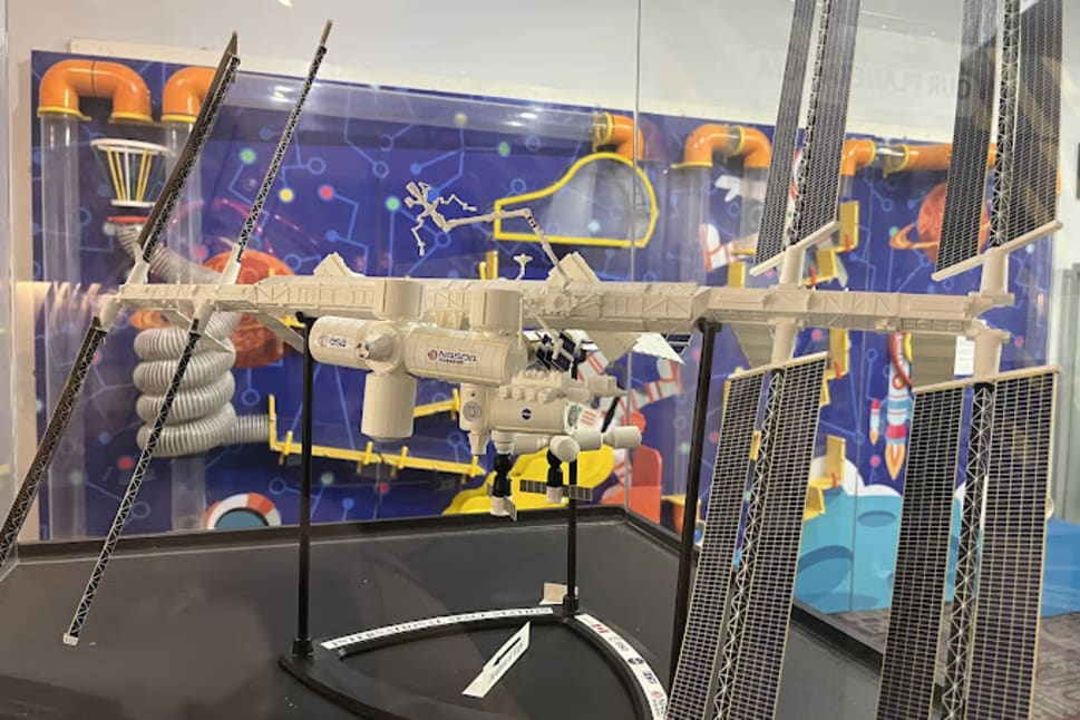A detailed model of a spacecraft with solar panels is displayed against a vibrant, science-themed backdrop in Vernon.