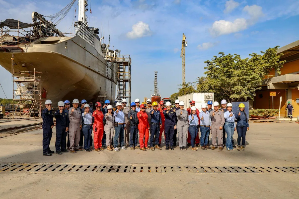 Grupo de trabajadores con casco frente a un barco en COTECMAR