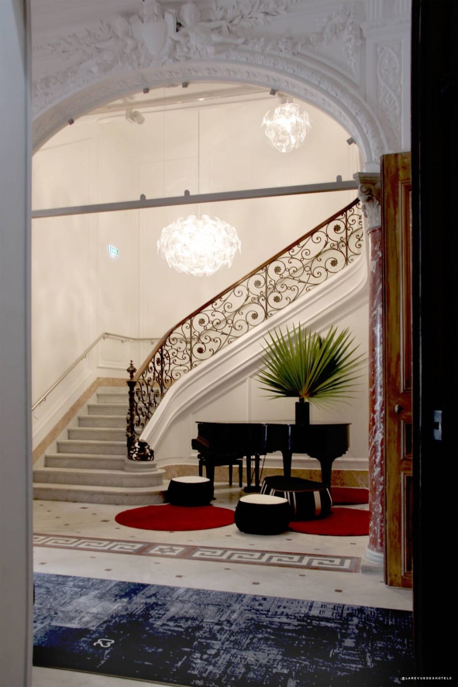19th-century grand staircase at Hôtel C2 with wrought-iron banister and grand piano