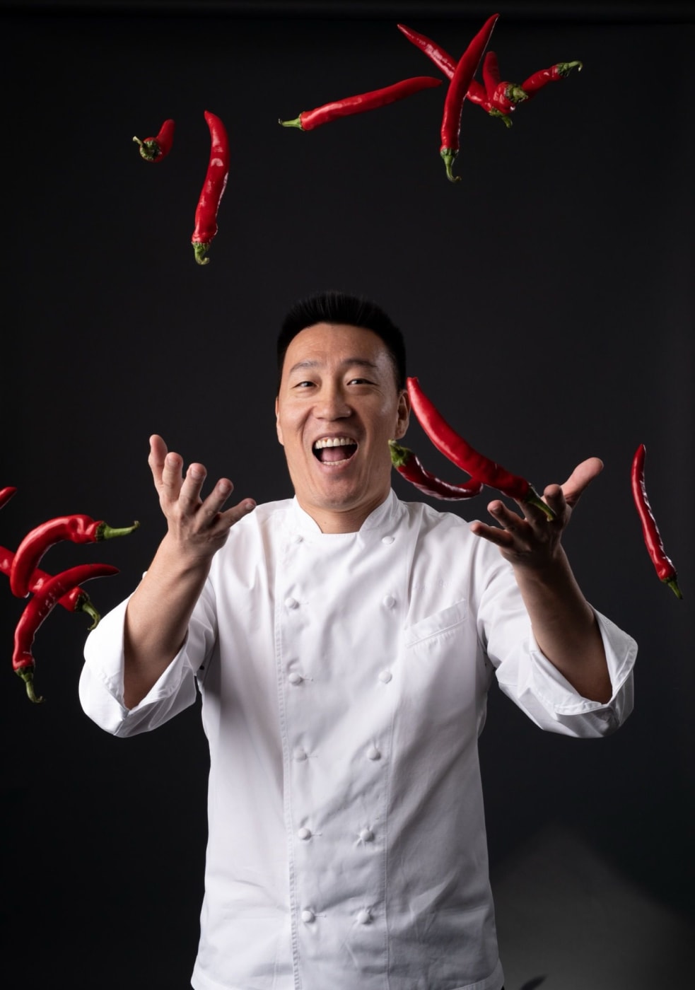 Chef Akira Back in a white jacket tossing red chillies