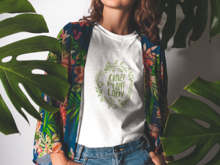 Junge Frau mit weißem T-Shirt mit grünem Aufdruck "Crazy Plant Lady" zwischen Monstera-Blättern