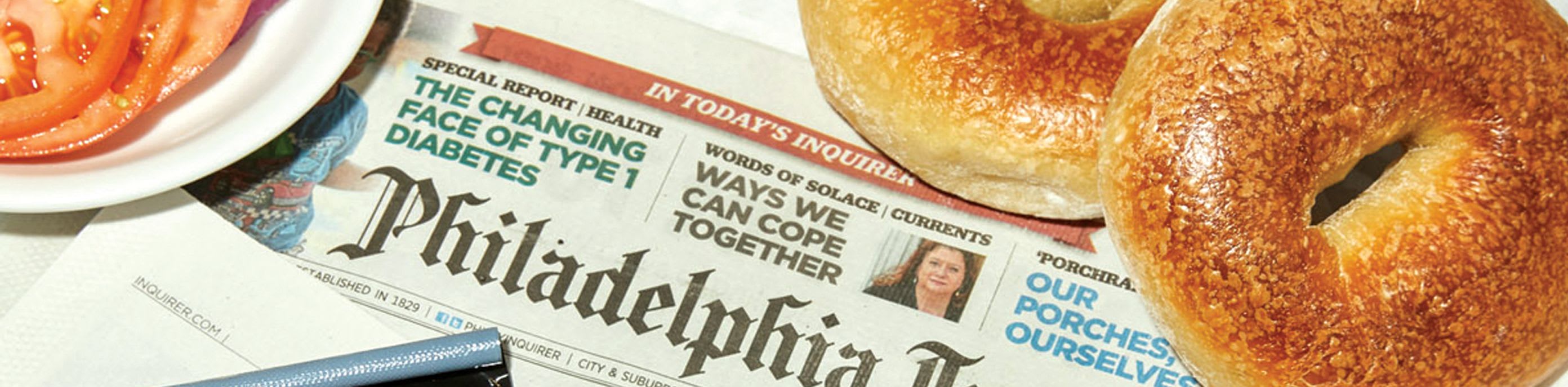 A picture three of our bagels, along with some tomatoes and onions, on top of a copy of the Philadelphia Inquirer. 