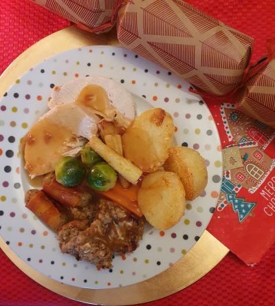 A dinner plate with a Christmas dinner next to a cracker and Christmas napkin