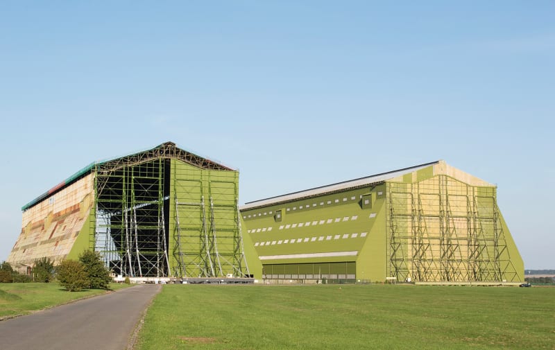 Sheds 1 and 2 of the former Royal Airship Works at Cardington: photo from Wikipedia, by liboharz. The black dot by the Shed at extreme right is a car