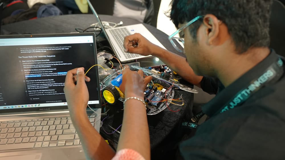 Students debugging a hardware build together at a table, laptop open to assembly instructions
