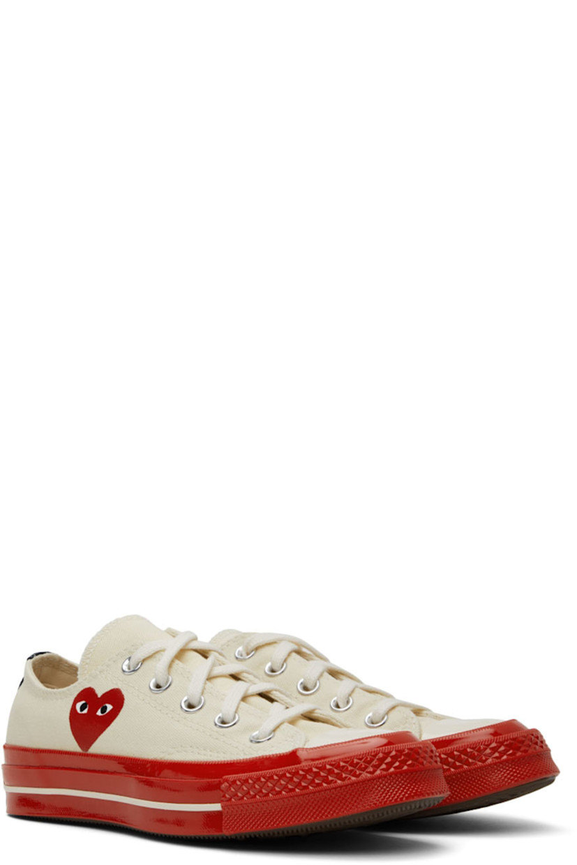 Low-top canvas sneakers in off-white.

· Round rubber cap toe
· Lace-up closure
· Logo graphic printed at outer side
· Eyelet vents at inner side
· Webbing trim in black at heel
· Logo embossed at heel 
· Rubber midsole in red
· Treaded rubber outsole in brown

Part of the Comme des Garçons Play x Converse collaboration.

Supplier color: Off white