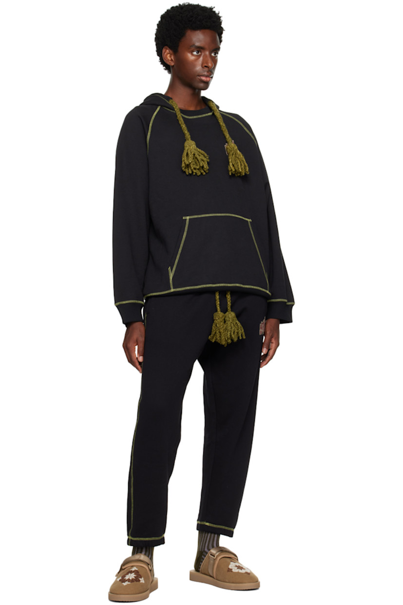 Cotton-blend fleece hoodie. 

· Hand-woven awassi wool Bedouin tassels at hood
· Hand-stitched tatreez embroidery at chest
· Kangaroo pocket
· Rib knit hem and cuffs
· Raglan sleeves
· Contrast stitching in green

Supplier color: Black