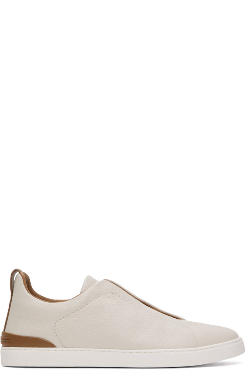 Low-top grained deerskin slip-on sneakers in off-white and tan.

· Elasticized criss-crossing straps at vamp
· Logo embossed at padded tongue
· Padded collar
· Pull-loop at heel collar
· Rubberized logo patch at heel counter
· Cushioned Sanitized® insole
· Buffed leather lining
· Treaded rubber sole

Supplier color: Off white