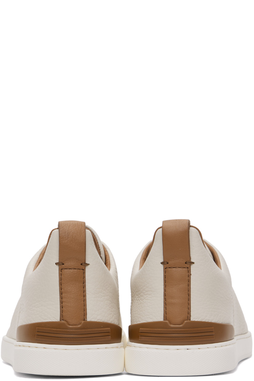 Low-top grained deerskin slip-on sneakers in off-white and tan.

· Elasticized criss-crossing straps at vamp
· Logo embossed at padded tongue
· Padded collar
· Pull-loop at heel collar
· Rubberized logo patch at heel counter
· Cushioned Sanitized® insole
· Buffed leather lining
· Treaded rubber sole

Supplier color: Off white