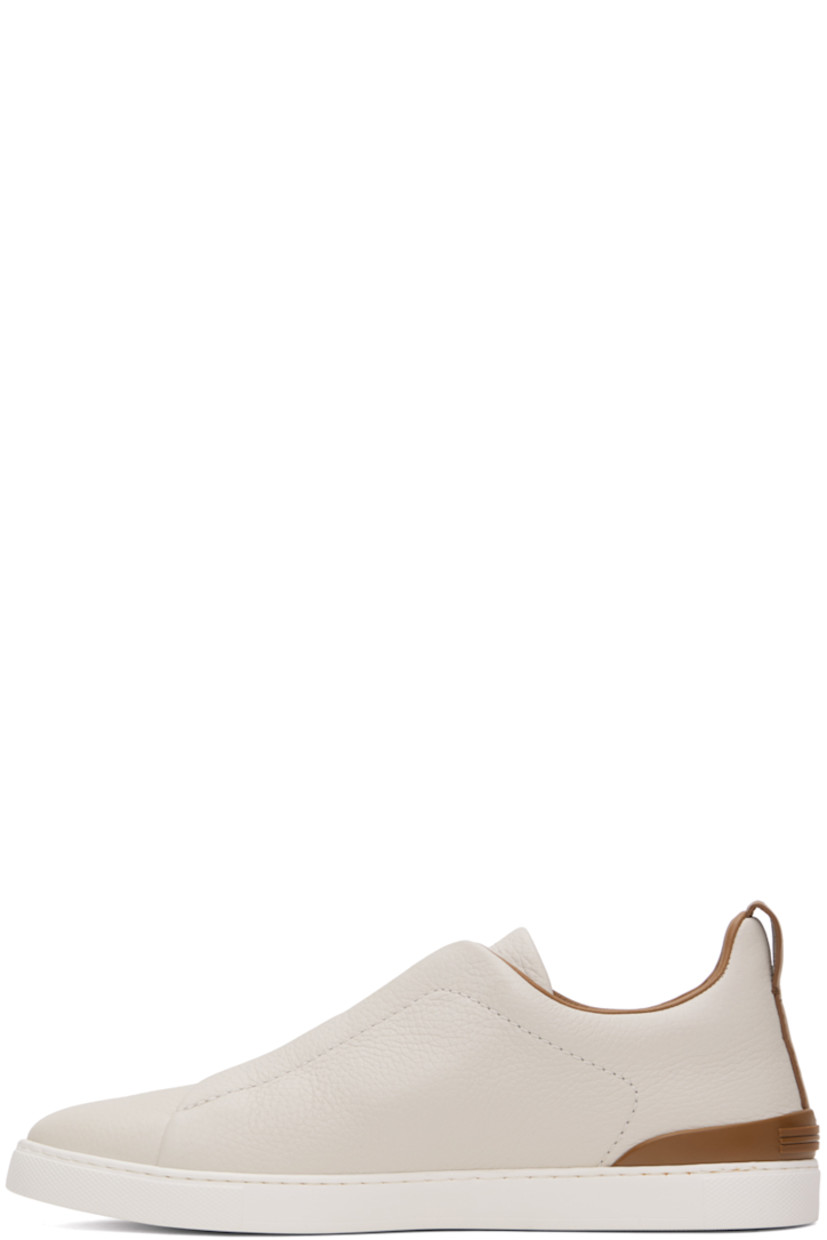 Low-top grained deerskin slip-on sneakers in off-white and tan.

· Elasticized criss-crossing straps at vamp
· Logo embossed at padded tongue
· Padded collar
· Pull-loop at heel collar
· Rubberized logo patch at heel counter
· Cushioned Sanitized® insole
· Buffed leather lining
· Treaded rubber sole

Supplier color: Off white