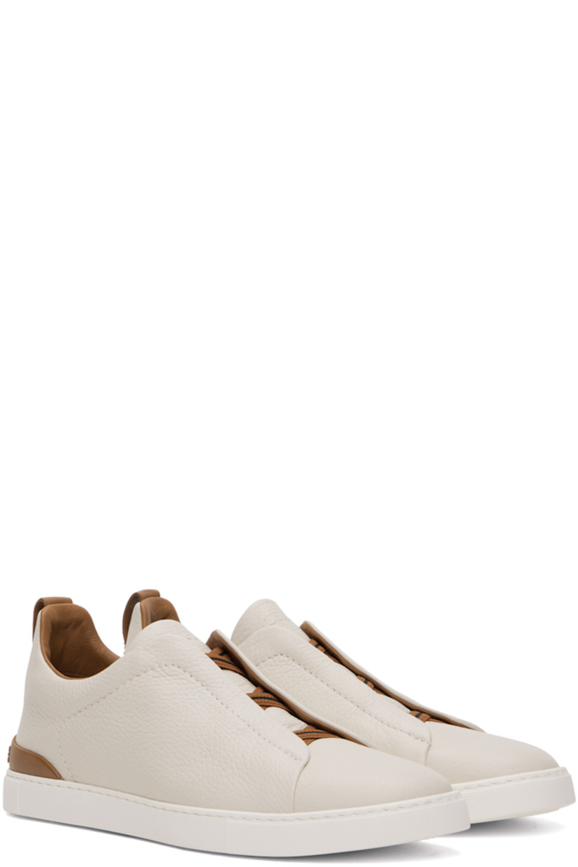 Low-top grained deerskin slip-on sneakers in off-white and tan.

· Elasticized criss-crossing straps at vamp
· Logo embossed at padded tongue
· Padded collar
· Pull-loop at heel collar
· Rubberized logo patch at heel counter
· Cushioned Sanitized® insole
· Buffed leather lining
· Treaded rubber sole

Supplier color: Off white