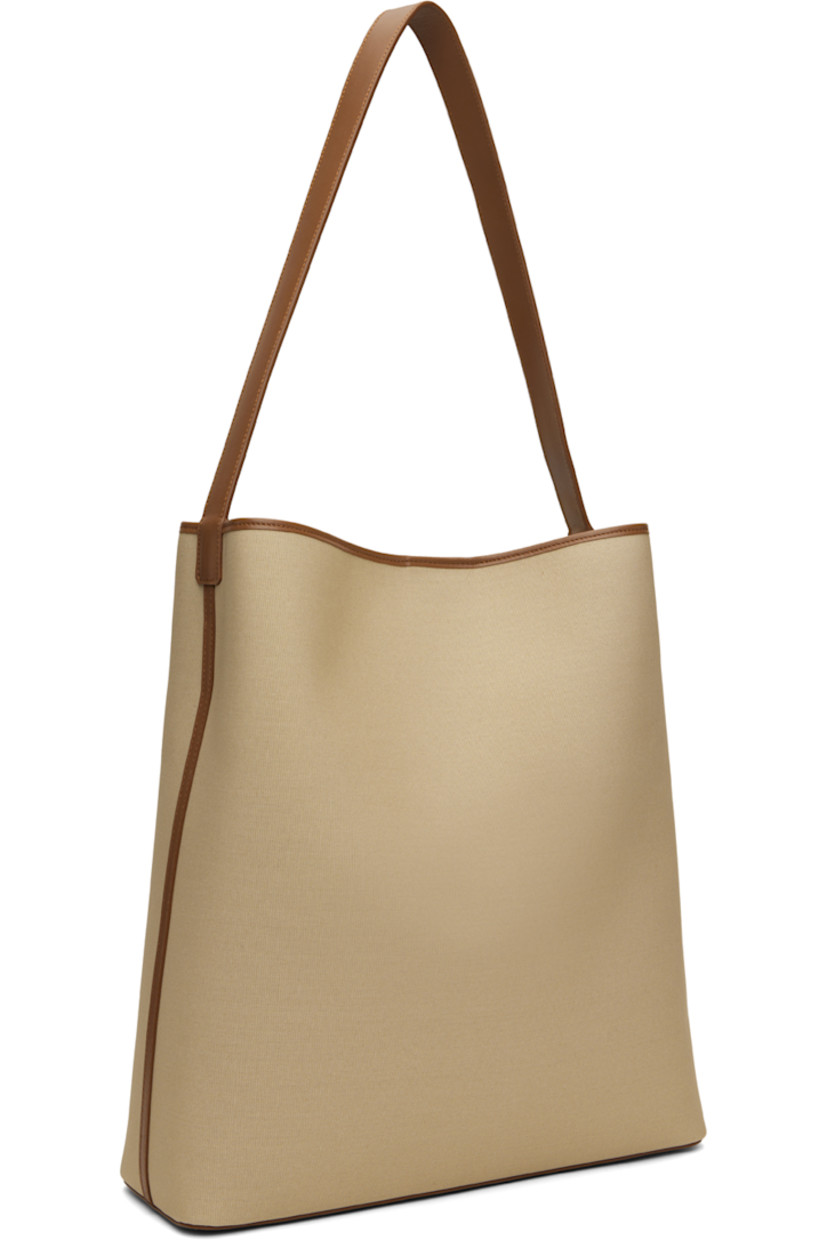 Canvas tote in beige.

· Buffed calfskin trim throughout
· Fixed shoulder strap
· Bumper studs at base
· Magnetic closure
· Laptop compartment at interior
· Grained faux-leather lining
· H14.5" x W13.25" x D4.25"

Supplier color: Canvas
