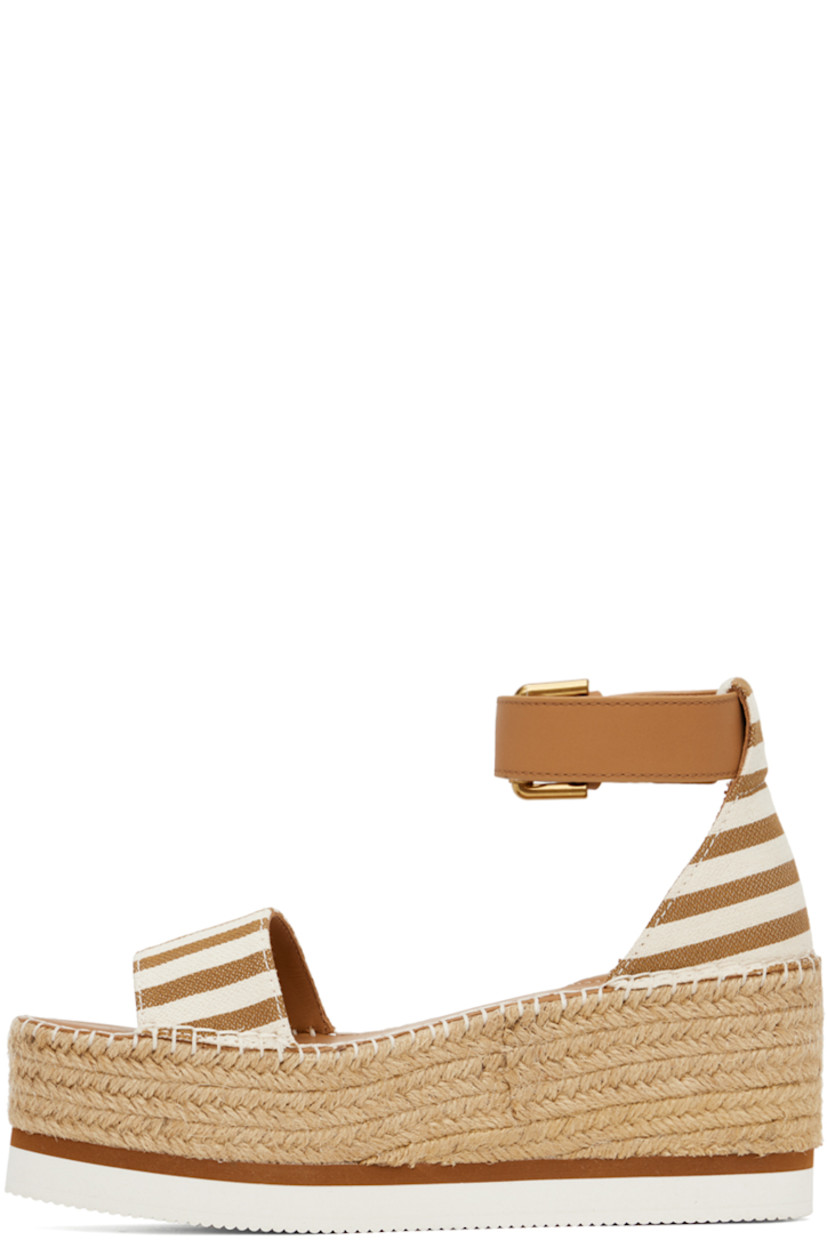 Canvas flat sandals in tan and white.

· Open toe
· Calfskin pin-buckle ankle strap
· Buffed calfskin footbed
· Blanket stitching at welt
· Braided jute platform midsole
· Treaded foam rubber sole
· Platform: H2.25"

Supplier color: Tan