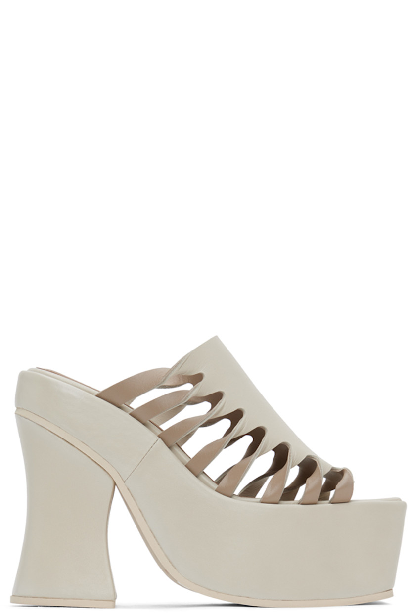 Buffed leather mules in off-white.

· Open square toe
· Twisted detailing and cutouts at sides 
· Logo embossed at padded footbed
· Covered block heel 
· Platform midsole
· Foam rubber sole
· Platform: H2.25" 
· Heel: H5"

Supplier color: Off-white mix