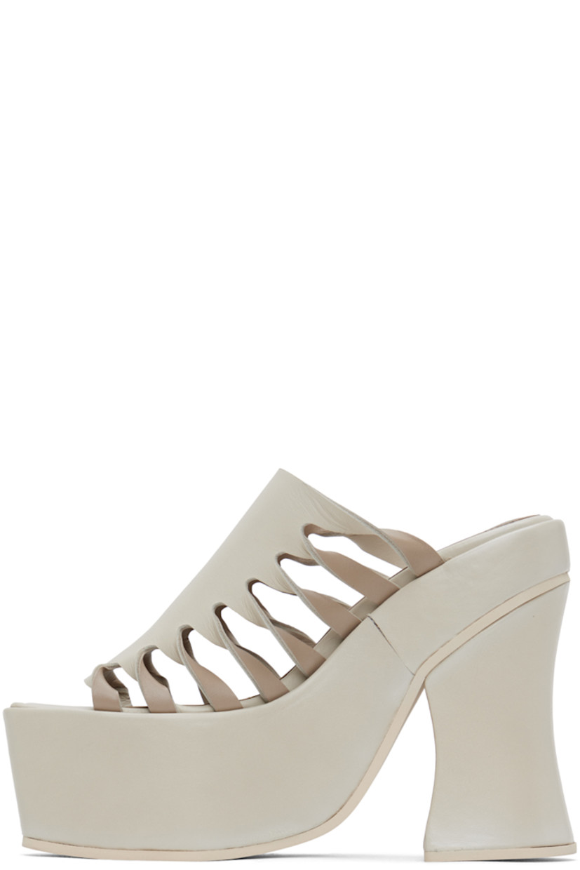 Buffed leather mules in off-white.

· Open square toe
· Twisted detailing and cutouts at sides 
· Logo embossed at padded footbed
· Covered block heel 
· Platform midsole
· Foam rubber sole
· Platform: H2.25" 
· Heel: H5"

Supplier color: Off-white mix