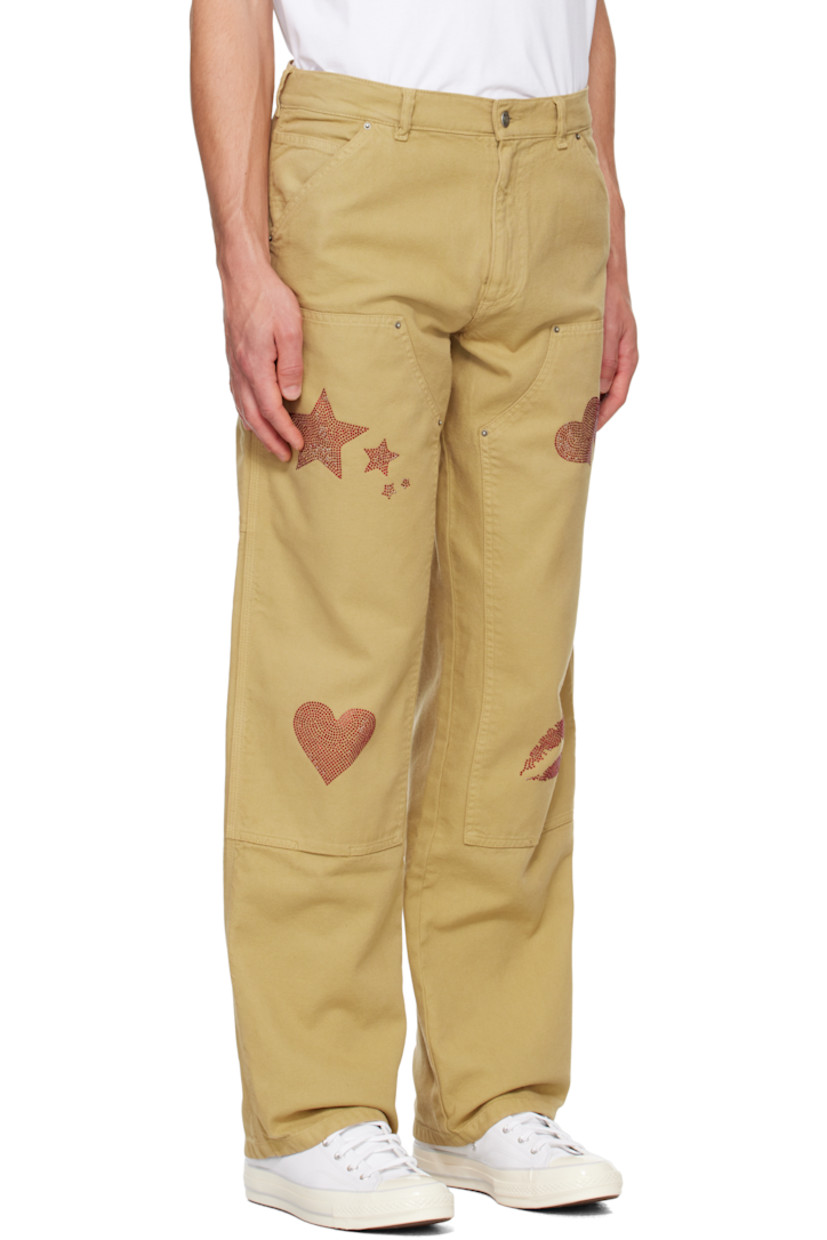 Deadstock cotton canvas trousers. 

· Belt loops
· Five-pocket styling 
· Zip-fly 
· Panel at knees
· Crystal-cut graphics at legs
· Hammer loop at outseam
· Patch pockets at outseams
· Crystal-cut logo graphic at back pocket

Featuring artwork by Vanna Youngstein.

Supplier color: Dark beige