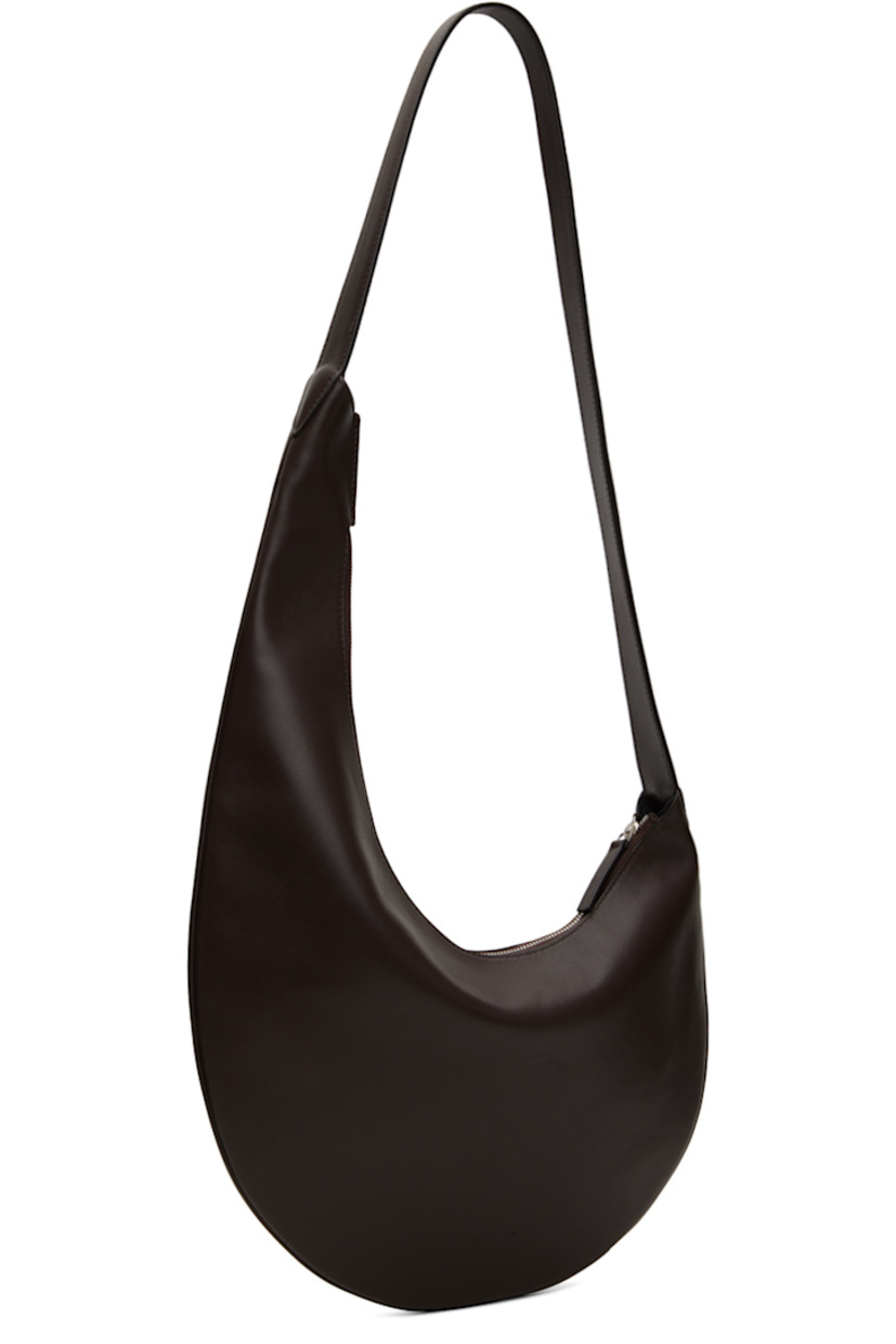 Buffed calfskin shoulder bag in brown. 

· Piping throughout 
· Fixed shoulder strap
· Logo embossed at face
· Zip closure
· Patch pocket at interior 
· Faille lining
· H6.5" x W10" 
· Total height: H26.5"

Supplier color: Dark chocolate
