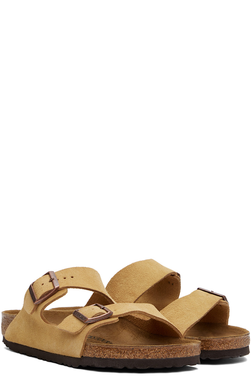 Suede slip-on sandals in beige. 

· Open toe
· Adjustable pin-buckle straps at vamp
· Logo embossed at inner side
· Logo stamp at molded suede footbed
· Cork midsole
· Treaded EVA rubber sole
· Logo-engraved copper-tone hardware

Supplier color: Latte cream suede