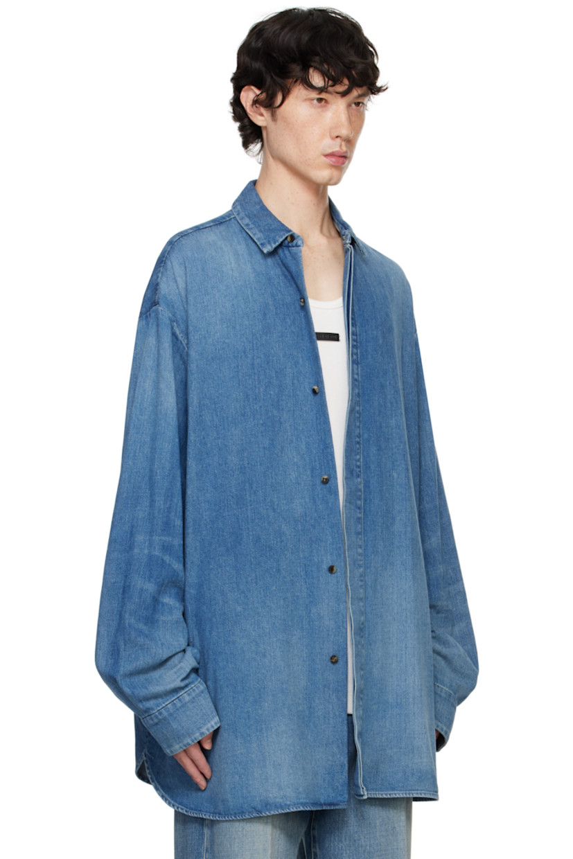 Oversized non-stretch denim shirt. Fading throughout.

· Spread collar
· Concealed button closure
· Shirttail hem
· Dropped shoulders
· Pleated single-button barrel cuffs
· Leather logo patch at back 
· Storm flap at back yoke
· Horn hardware

Supplier color: Medium indigo