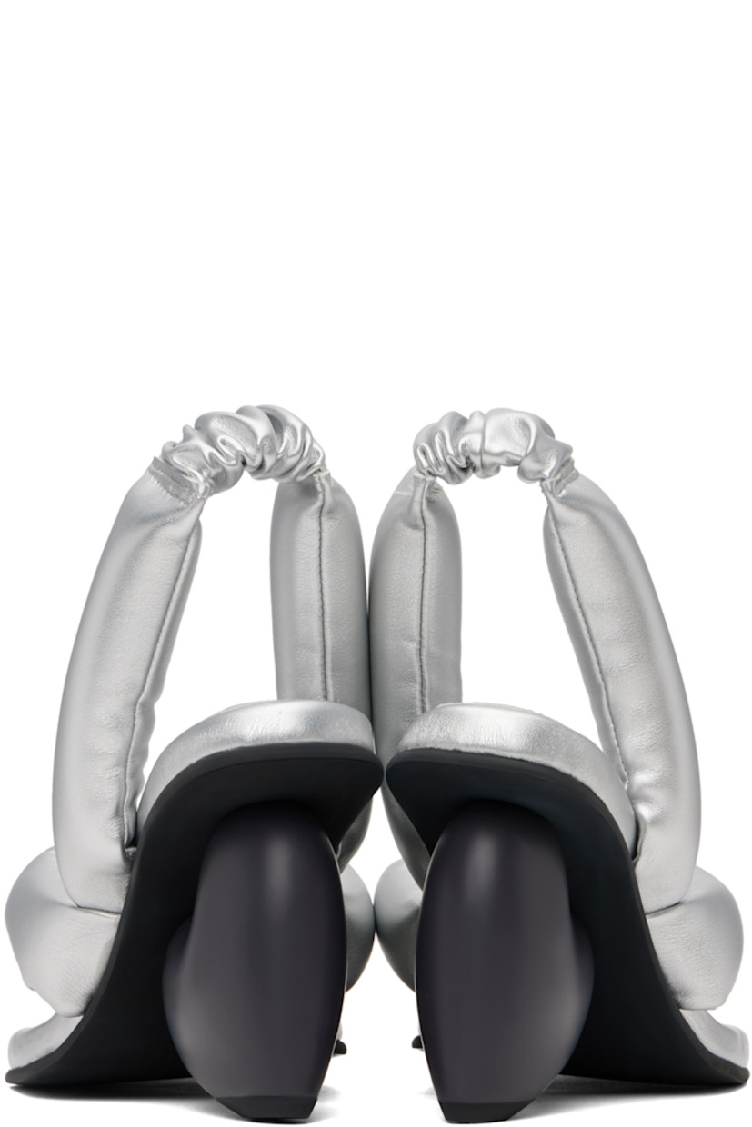 Padded buffed faux-leather heeled sandals in metallic silver tone. 

· Open square toe
· Thong-style strap at vamp
· Partially elasticized slingback strap 
· Logo embossed at padded footbed
· Sculptural heel with rubber injection
· Treaded rubber sole
· Heel: H3.25"

Supplier color: Silver vegan leather