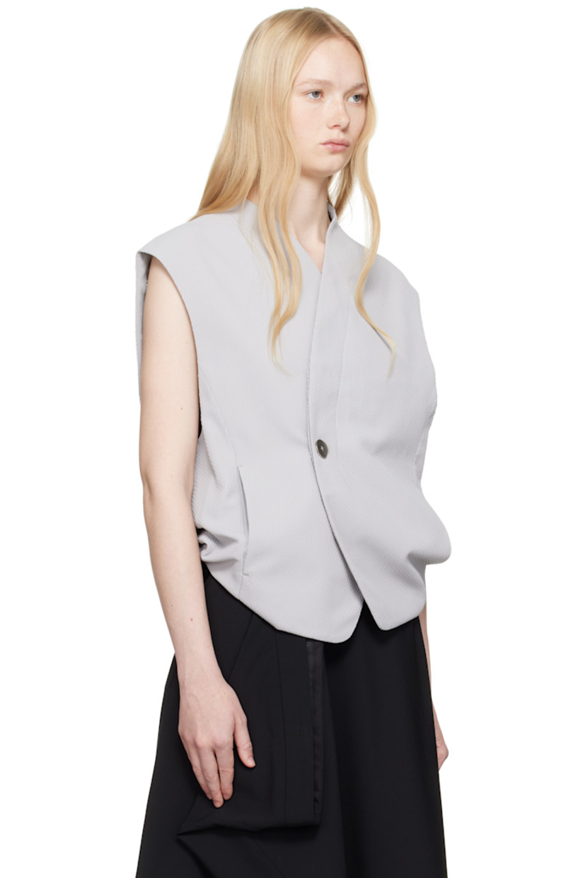 Polyester dobby cloth vest.

· V-neck
· Offset button closure
· Darts at collar
· Seam pockets
· Frayed flag with topstitching at back
· Tucks and draping at back
· Exposed lining at back hem
· Welt pocket at interior
· Full logo-woven satin lining

Supplier color: Grey
