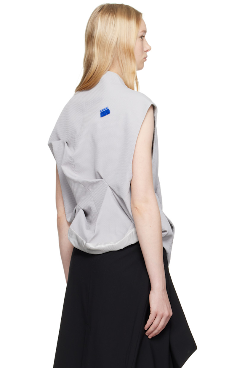 Polyester dobby cloth vest.

· V-neck
· Offset button closure
· Darts at collar
· Seam pockets
· Frayed flag with topstitching at back
· Tucks and draping at back
· Exposed lining at back hem
· Welt pocket at interior
· Full logo-woven satin lining

Supplier color: Grey