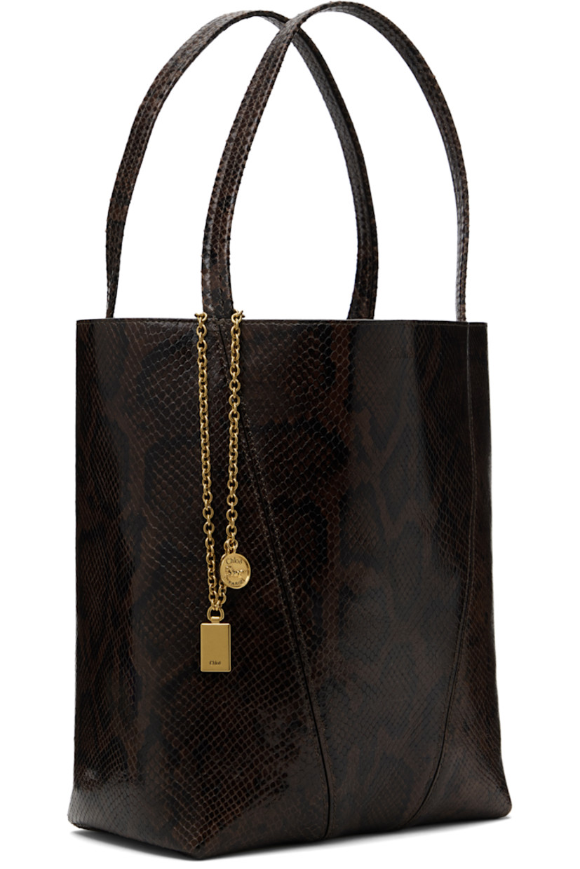 Snake-embossed goatskin tote in brown.

· Twin carry handles
· Detachable logo charms at handle 
· Logo stamp at face
· Lanyard clasp at interior
· Calfskin suede lining
· Gold-tone hardware
· H12" x W10.5" x D5.5"

Supplier color: Sooty brown
