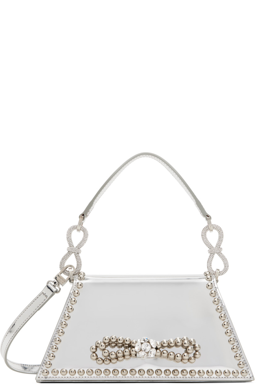 Patent leather top handle bag in silver tone.

· Studs throughout
· Detachable carry handle
· Crystal-cut bow accents at carry handle
· Adjustable and detachable crossbody strap
· Bow accent at face 
· Magnetic press-stud flap 
· Card slot at interior
· Twill lining 
· Logo-engraved silver-tone hardware
· H4.5" x W9.5" x D2"

Supplier color: Silver