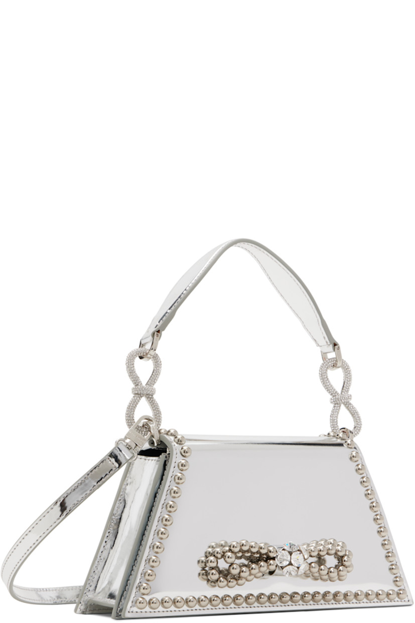 Patent leather top handle bag in silver tone.

· Studs throughout
· Detachable carry handle
· Crystal-cut bow accents at carry handle
· Adjustable and detachable crossbody strap
· Bow accent at face 
· Magnetic press-stud flap 
· Card slot at interior
· Twill lining 
· Logo-engraved silver-tone hardware
· H4.5" x W9.5" x D2"

Supplier color: Silver