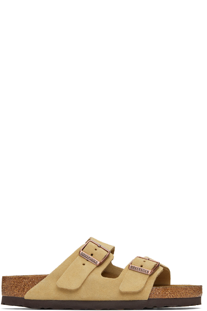 Suede slip-on sandals in beige. 

· Open toe
· Pin-buckle straps at vamp
· Logo embossed at inner side
· Logo printed at molded footbed
· Suede lining
· Cork-latex midsole
· Treaded rubber sole
· Logo-engraved antiqued brass-tone hardware

Supplier color: Latte cream