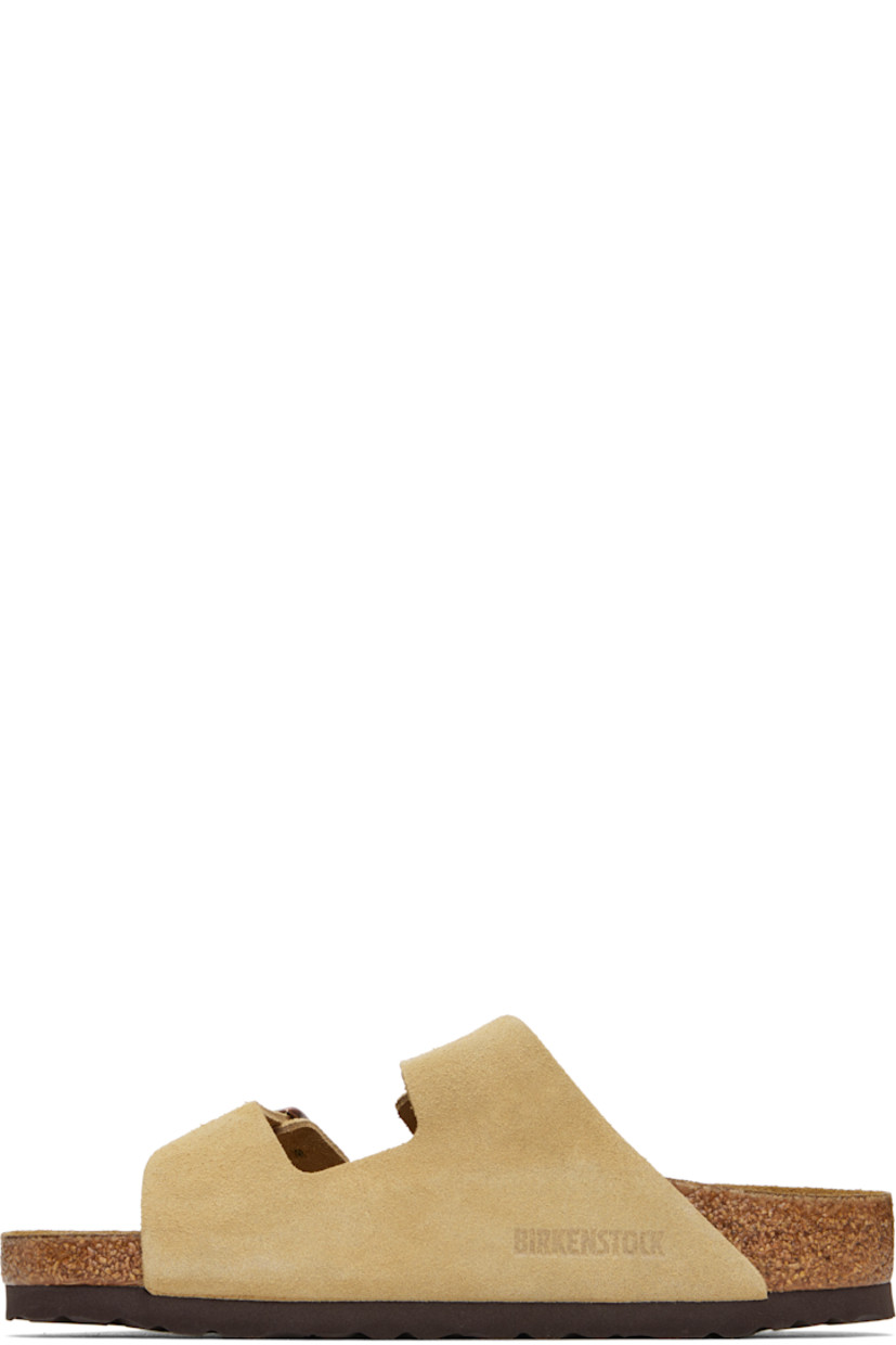 Suede slip-on sandals in beige. 

· Open toe
· Pin-buckle straps at vamp
· Logo embossed at inner side
· Logo printed at molded footbed
· Suede lining
· Cork-latex midsole
· Treaded rubber sole
· Logo-engraved antiqued brass-tone hardware

Supplier color: Latte cream