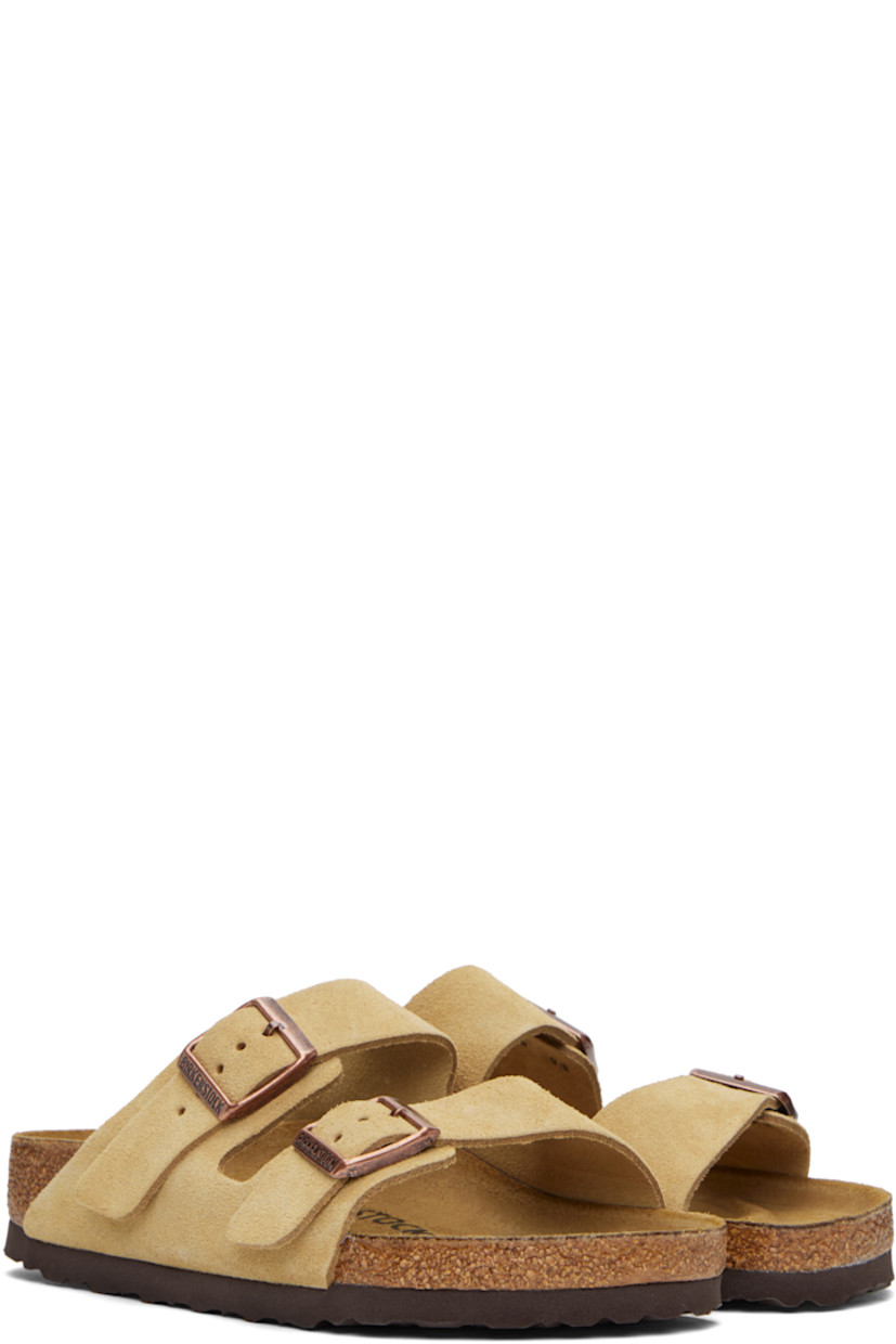 Suede slip-on sandals in beige. 

· Open toe
· Pin-buckle straps at vamp
· Logo embossed at inner side
· Logo printed at molded footbed
· Suede lining
· Cork-latex midsole
· Treaded rubber sole
· Logo-engraved antiqued brass-tone hardware

Supplier color: Latte cream